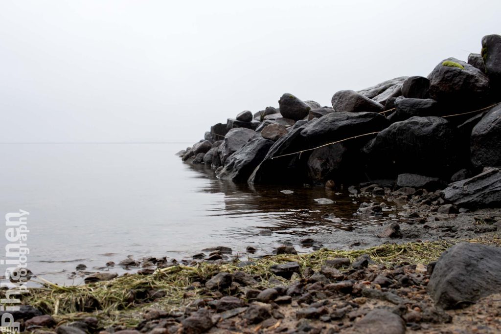 Rantakivikko Oulujärven rannassa. Taustalla vesisateen suttaama harmaa horisontti.