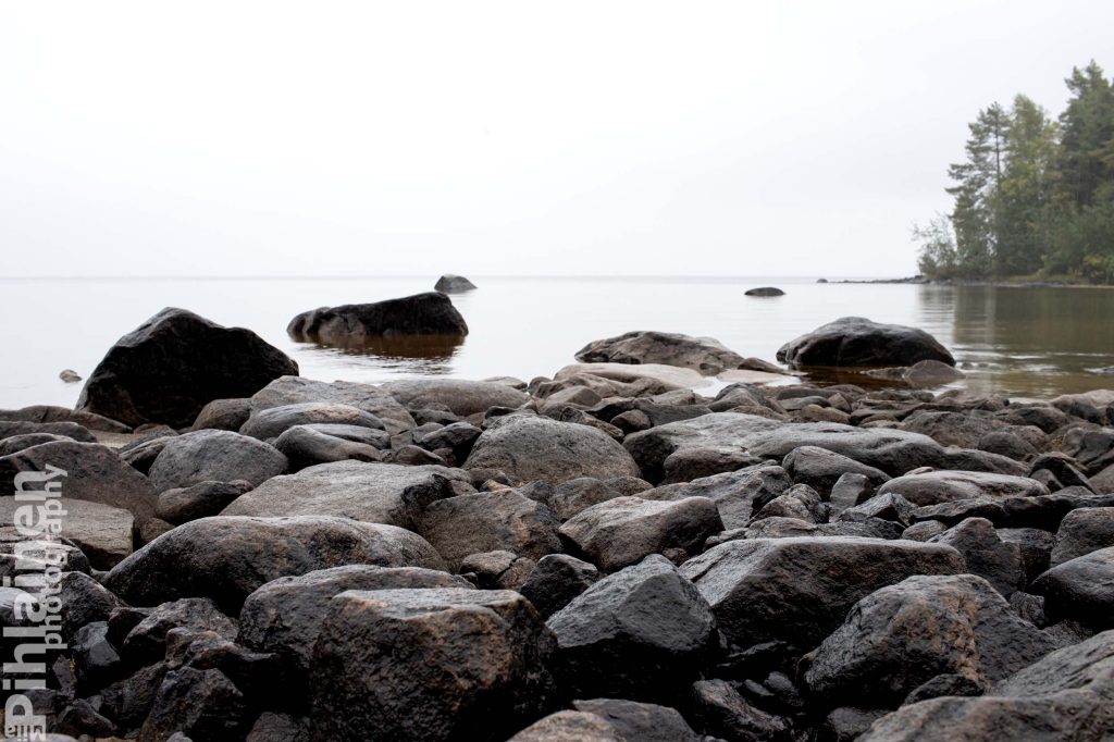 Rantakivikko Oulujärven rannassa. Taustalla vesisateen suttaama harmaa horisontti.