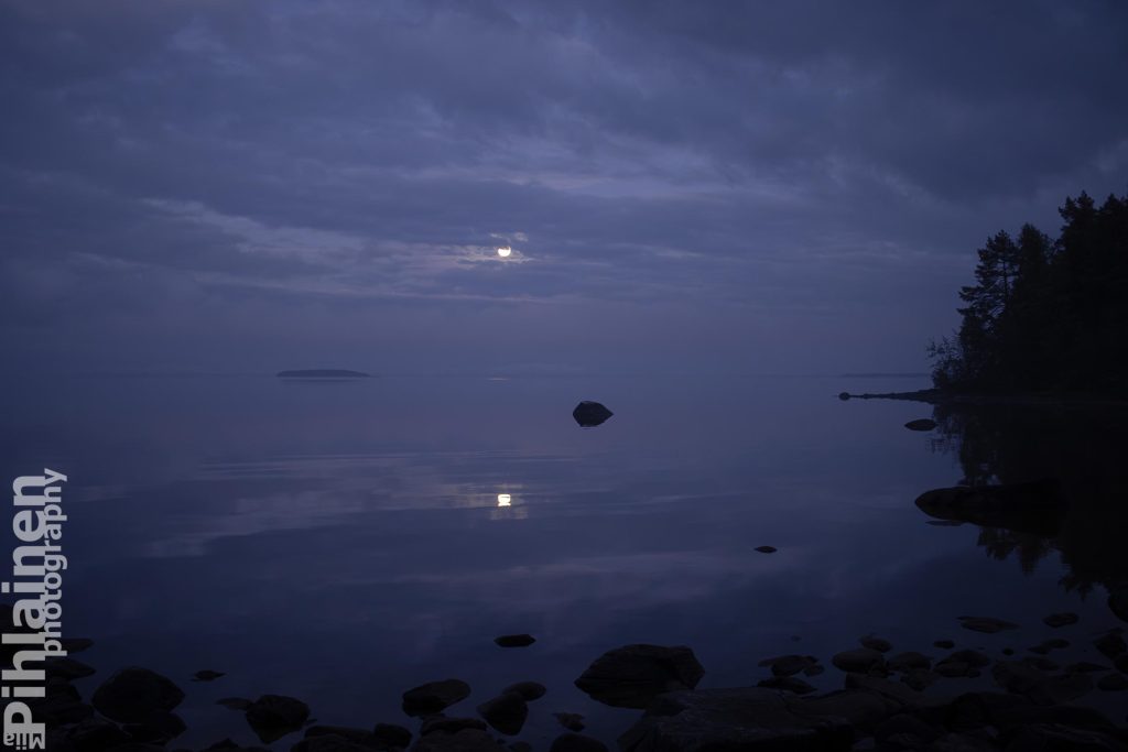 Tyyni Oulujärvi illalla. Pilven raosta loistaa kuu, joka heijastuu järvenpinnasta.