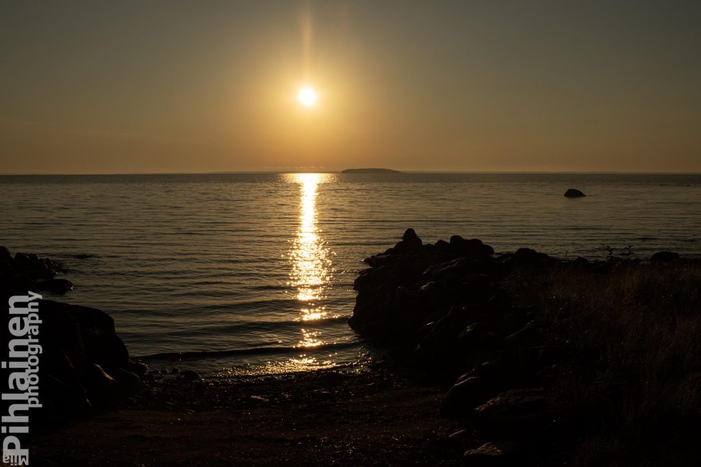 Aamuaurinko paistaa matalalta ja heijastuu järvenpinnasta.